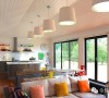 白色灯芯绒沙发和黄色、粉色、橙色的布艺抱枕搭配，构造温暖和谐的客厅。一排吊灯依次悬挂在天花板上，烘托出明亮雅致的空间氛围。大落地窗，采光极佳。
