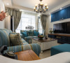在客厅区域中设计师用蓝色布艺沙发，木制茶几、边几，地中海风格的吊灯整体搭配，体现地中海风格的色彩结合了海与天明亮，在简单中也能体会到丰富。